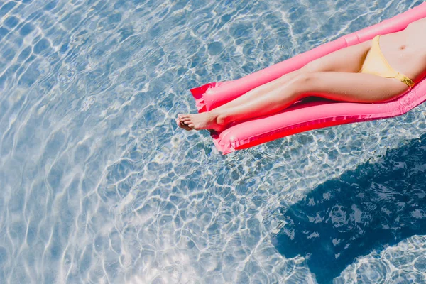 Cropped view of sexy slim woman in swimsuit swimming on pink pool float in swimming pool — Stock Photo