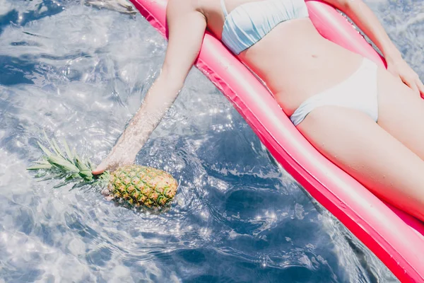 Vista ritagliata della donna che nuota sulla piscina rosa galleggiante con ananas in piscina — Foto stock