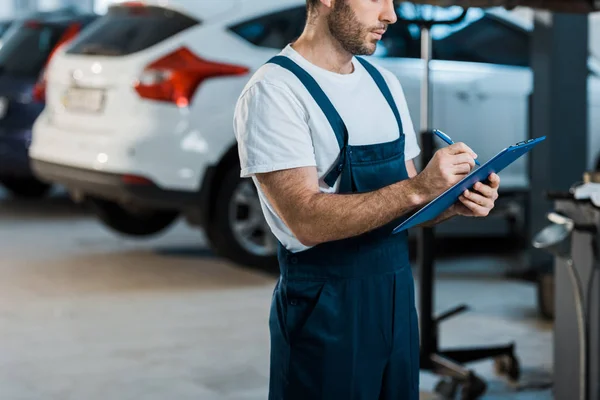 Vista ritagliata di scrittura meccanico auto tenendo appunti vicino alle auto — Stock Photo