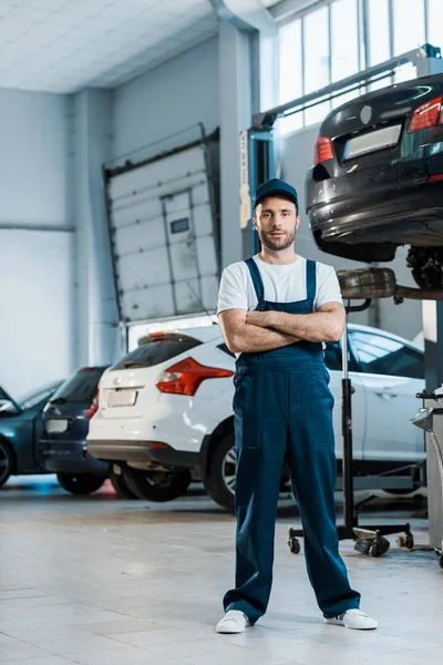 Schöner Automechaniker, der mit verschränkten Armen neben Autos steht — Stockfoto