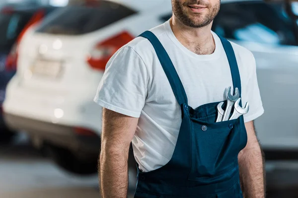 Vue recadrée du mécanicien de voiture heureux debout avec clés à main dans la poche — Photo de stock