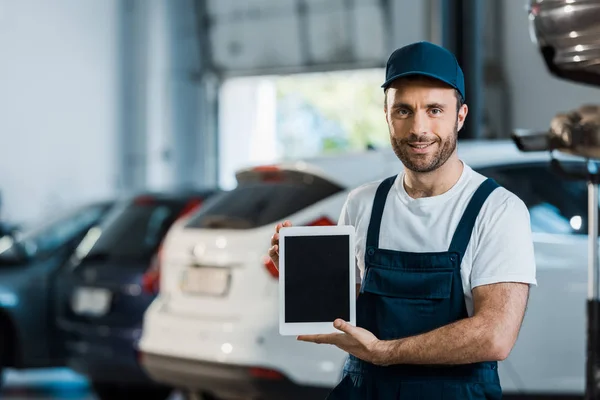 Mecánico alegre del coche que sostiene la tableta digital con la pantalla en blanco en servicio del coche - foto de stock