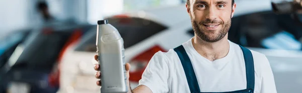 Panoramic shot of happy car mechanic holding bottle with car oil — Stock Photo