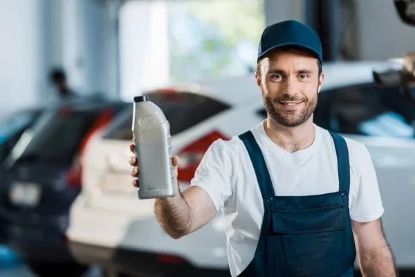 Mecánico del coche feliz en la botella de retención de la tapa con aceite de coche - foto de stock