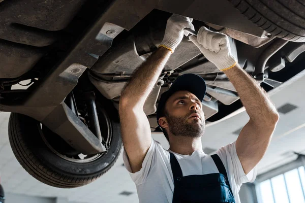 Low angle view of serious car mechanic repairing automobile in car service — Stock Photo