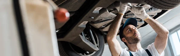 Panoramic shot of handsome auto mechanic repairing car — Stock Photo