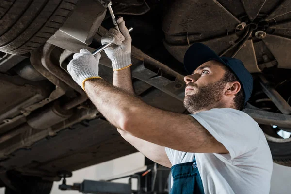 Low angle view of bearded car mechanic repairing automobile in car service — Stock Photo