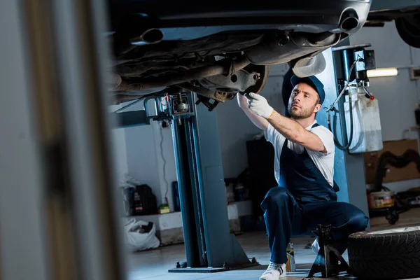 Selective focus of auto mechanic in cap and gloves repairing automobile in car service — Stock Photo