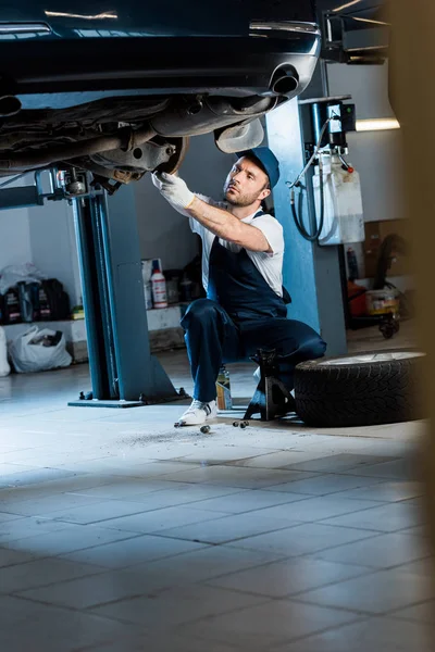 Handsome auto mechanic in cap repairing car in car service — Stock Photo