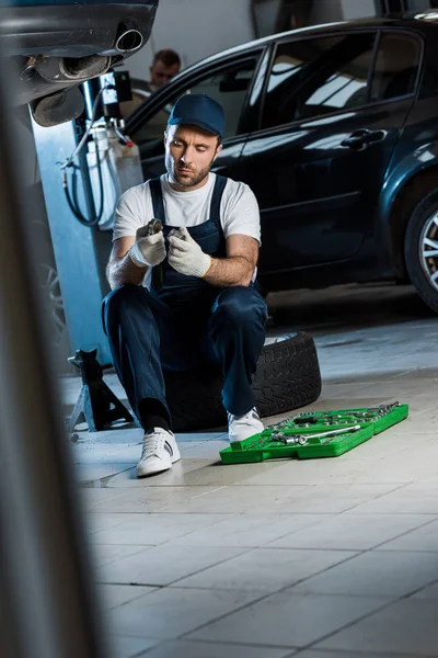 Enfoque selectivo de hombre barbudo guapo en la tapa mirando la caja de herramientas cerca de los coches - foto de stock