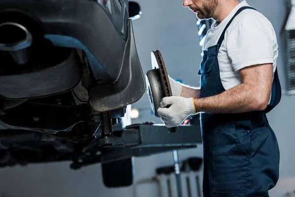 Cropped view of auto mechanic repairing automobile and holding car brake — Stock Photo