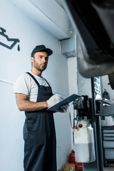 Selective focus of auto mechanic holding clipboard while looking at car — Stock Photo