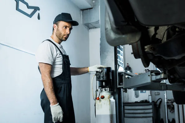 Messa a fuoco selettiva del meccanico automobilistico serio nel cappuccio che si leva in piedi vicino all'automobile nel servizio dell'automobile — Foto stock