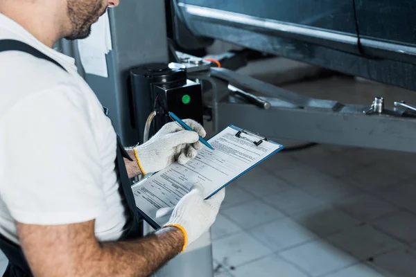 Cropped view of auto mechanic holding clipboard and pen — Stock Photo