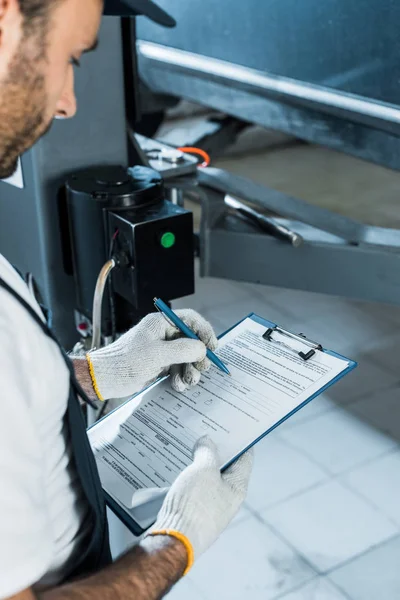 Cropped view of auto mechanic holding clipboard while writing in car service — Stock Photo