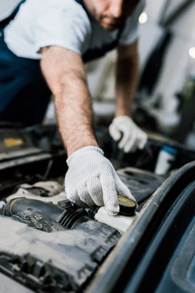 Cropped view of car mechanic touching cap in automobile — Stock Photo