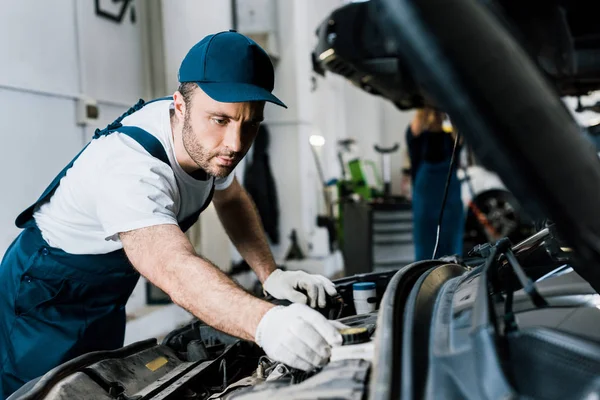 Selective focus of bearded car mechanic in gloves fixing automobile — Stock Photo