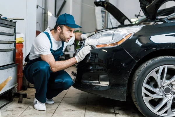 Schöner Automechaniker schaut auf Rücklicht in schwarzem Auto — Stockfoto