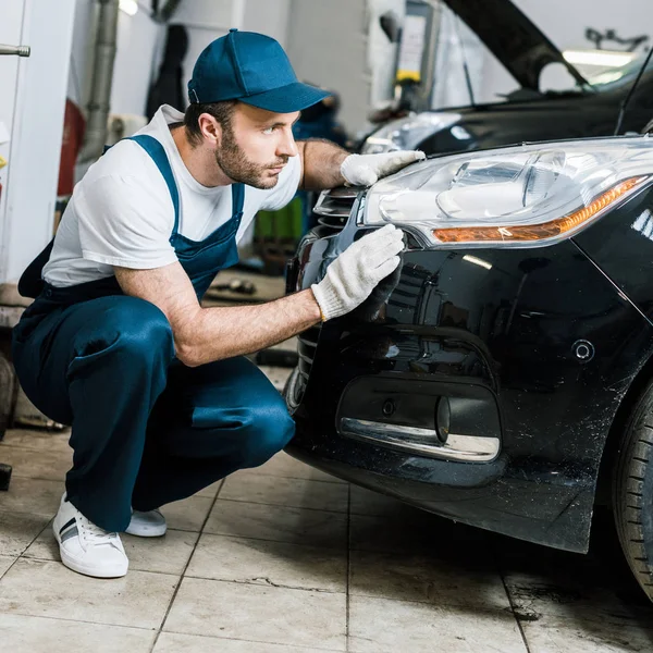 Handsome bearded car mechanic looking at tail light in black car — Stock Photo