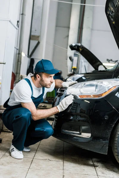 Handsome bearded auto mechanic looking at tail light in black car — Stock Photo