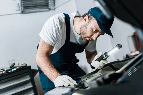 Selektiver Fokus des bärtigen Automechanikers mit Taschenlampe in der Nähe des Autos — Stockfoto