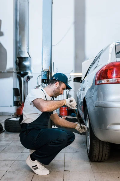 Bonito barbudo carro mecânico no uniforme mudança carro pneu no carro serviço — Fotografia de Stock