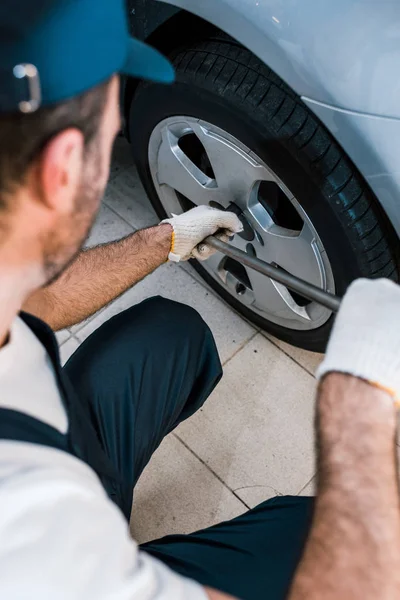 Cropped view of car mechanic in uniform holding metallic wrench near car — Stock Photo