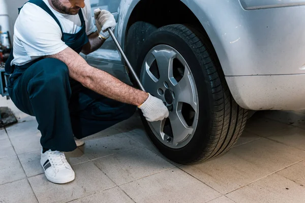 Cropped view of auto mechanic in uniform holding metallic wrench near car — Stock Photo