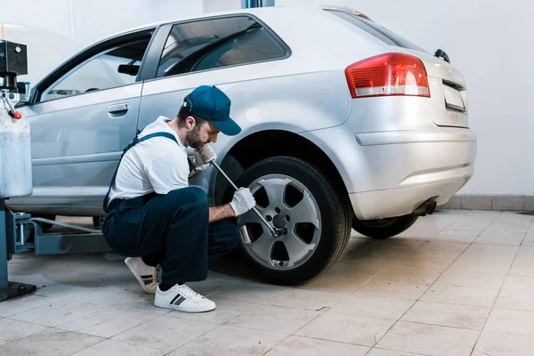 Bearded car mechanic in uniform changing car tire in car service — Stock Photo