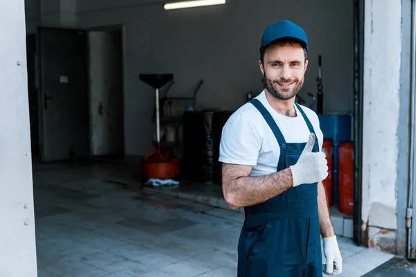 Handsome bearded car mechanic in cap standing and showing thumb up — Stock Photo