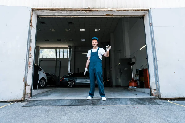 Happy bearded car mechanic holding keys near garage — Stock Photo