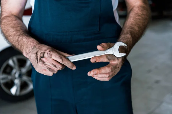 Cropped view of auto mechanic with mud on hands holding hand wrench in car repair station — Stock Photo