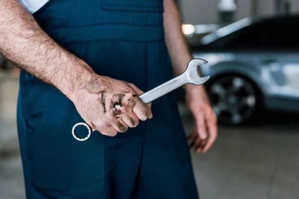 Cropped view of auto mechanic with mud on hand holding hand wrench in car repair station — Stock Photo