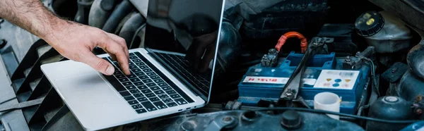 Panoramic shot of car mechanic using laptop with blank screen near car — Stock Photo