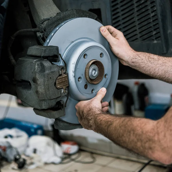 Cropped view of auto mechanic holding metallic car brake near auto — Stock Photo