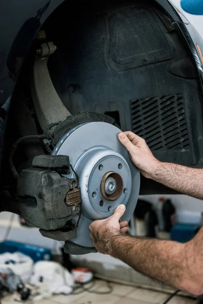 Cropped view of auto mechanic holding metallic car brake near automobile — Stock Photo