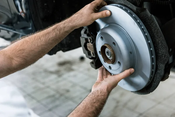 Cropped view of car mechanic holding metallic car brake near automobile — Stock Photo