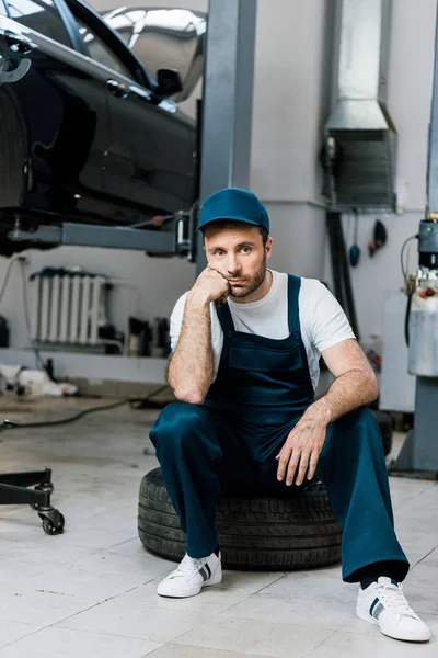 Hombre barbudo molesto mirando a la cámara y sentado en el neumático del coche - foto de stock