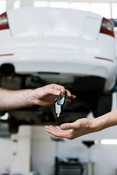 Cropped view of car mechanic giving key to man in garage — Stock Photo