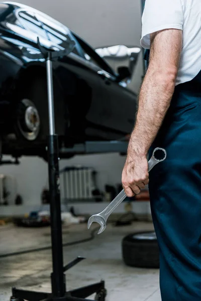 Cropped view of repairman holding hand wrench in car repair station — Stock Photo