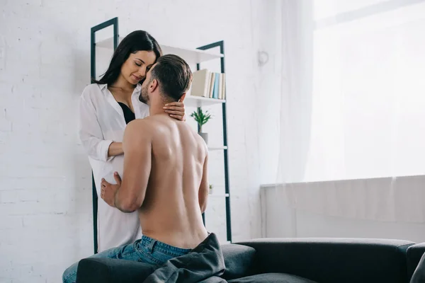 Mulher atraente e morena na camisa abraçando com homem sem camisa — Fotografia de Stock