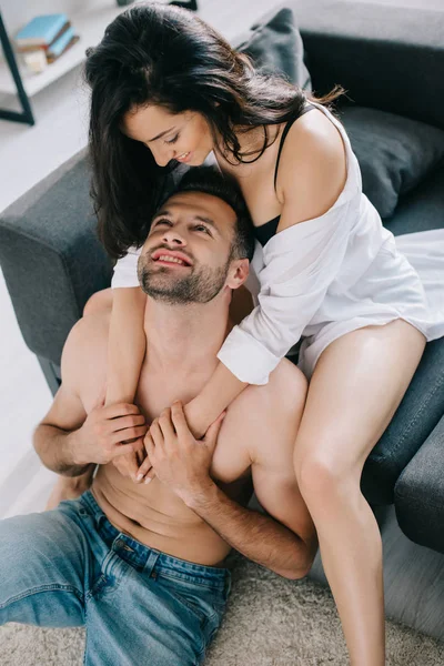 Mujer atractiva y morena en camisa abrazando y mirando al hombre - foto de stock