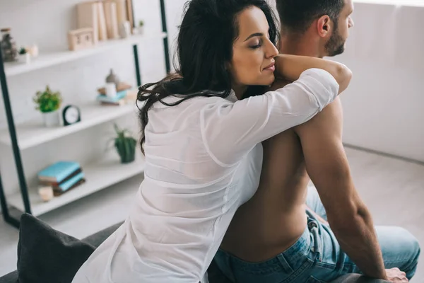 Atractiva y morena mujer con los ojos cerrados en camisa abrazando con el hombre - foto de stock