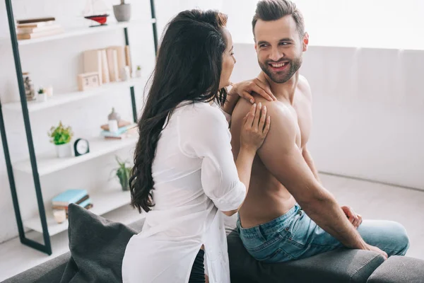 Mulher morena na camisa e homem bonito sentado no sofá e sorrindo — Fotografia de Stock