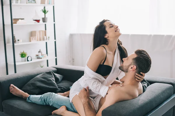 Hombre sin camisa y guapo abrazándose con morena y mujer sonriente en sujetador - foto de stock