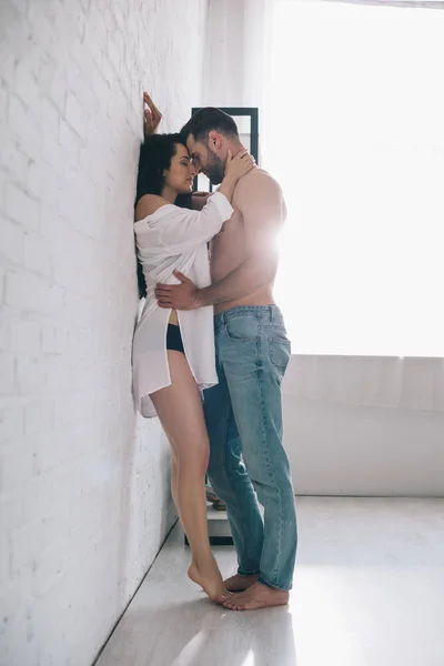 Sexy hombre abrazos y besos con morena mujer cerca de la pared - foto de stock