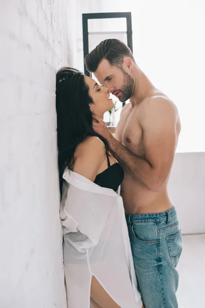 Сексуальний чоловік обіймає і цілує з брюнеткою і пристрасною жінкою біля стіни — стокове фото