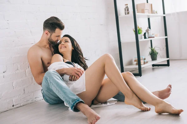 Сексуальна людина обійматися з брюнеткою і усміхнена жінка на підлозі — стокове фото