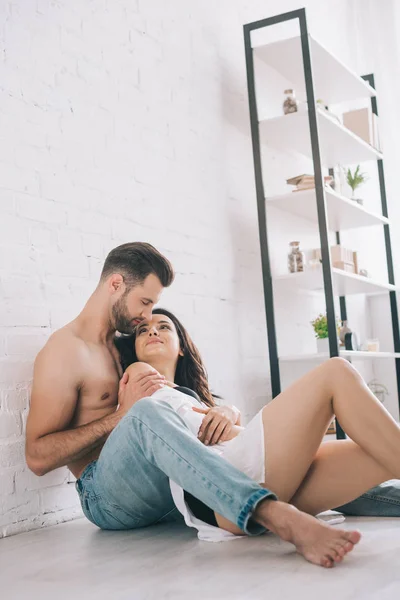 Сексуальна людина в джинсах обіймається з брюнеткою і привабливою жінкою на підлозі — стокове фото