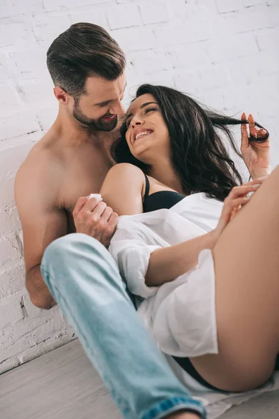 Sexy man in jeans hugging with brunette and smiling woman on floor — Stock Photo